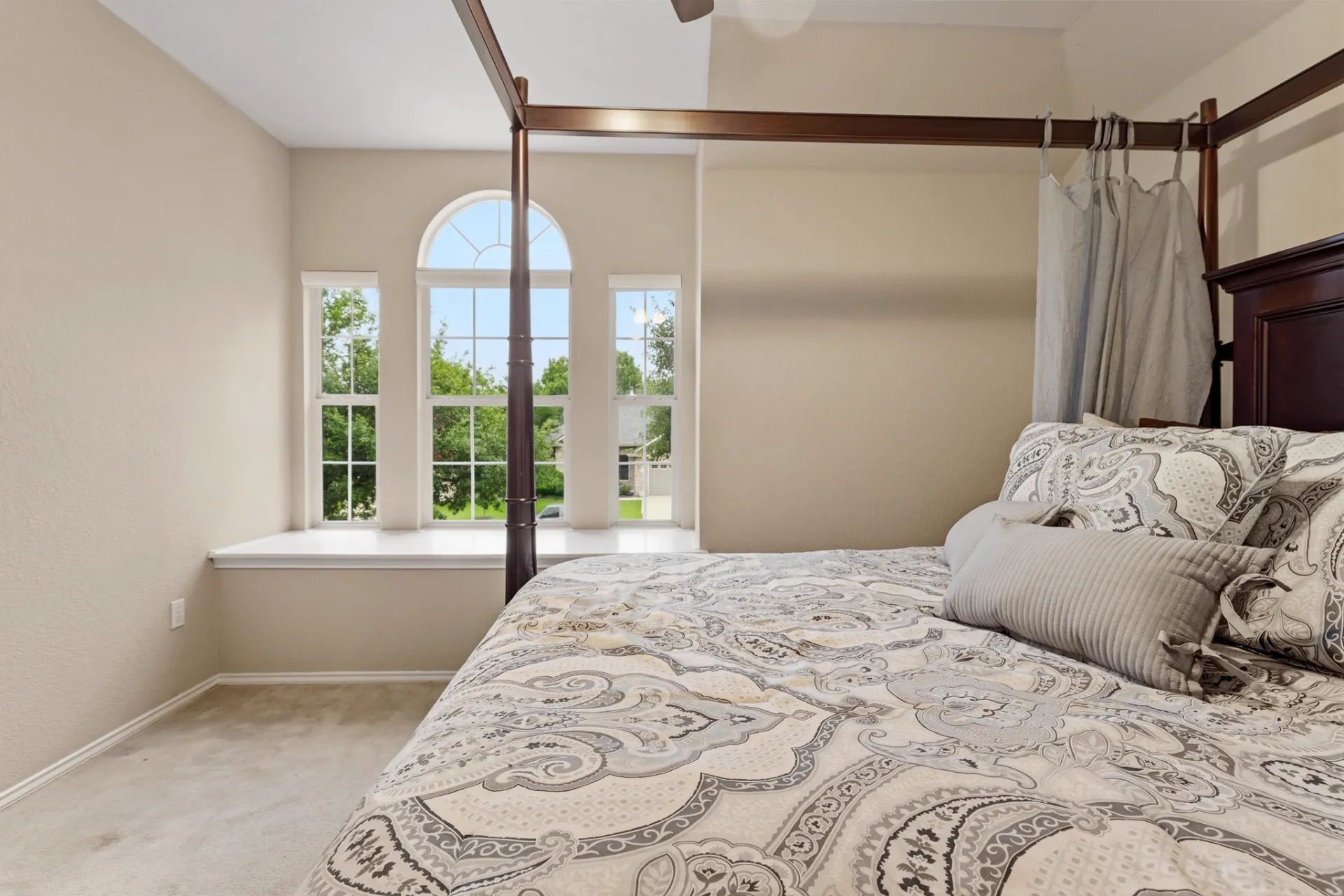 Guest bedroom arched window framing tree-lined neighborhood views
